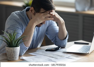 Distressed Young Caucasian Man Sit At Desk Paying Bills Feel Stressed Having Financial Problems. Unhappy Upset Millennial Male Frustrated By Debt Or Bankruptcy Managing Household Budget Or Expenses.