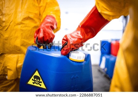 Distribution and transport of dangerous and hazardous chemicals. Close up view of plastic canister with toxic material carried by workers in protection suit. Foto stock © 