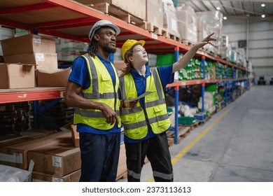 Distribution warehouse manager using tablet to check stock on storage shelf. Multiethnic man worker and colleague working together at storehouse discussing inventory as order. Diversity people talking