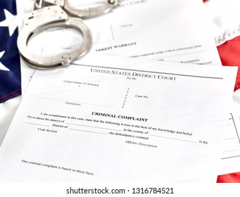 District Court Criminal Complaint, Arrest Warrant And Search And Seizure Warrant Doccuments On The American Flag With Handcuffs Isolated On White