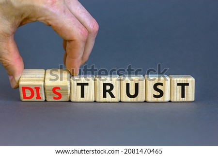 Distrust or trust symbol. Businessman turns wooden cubes, changes words 'distrust' to 'trust'. Beautiful grey table, grey background. Business and distrust or trust concept, copy space.