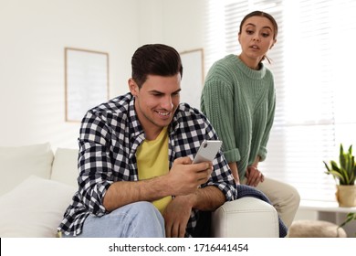 Distrustful Woman Peering Into Boyfriend's Smartphone At Home. Jealousy In Relationship