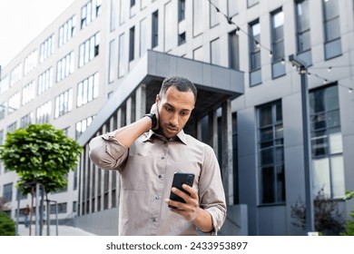 Disturbed arab man rubbing head with hand while looking at mobile phone screen on background of office building. Stressed manager leaving corporate workplace and receiving text message from boss. - Powered by Shutterstock