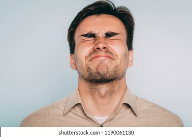 disturbed facial expression. grimace of pain. unbearable suffering and torture. man with eyes shut. portrait of a young brunet guy on light background. emotion feelings and reaction concept.