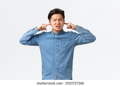 Disturbed And Frustrated Asian Man Complaining Loud Noise, Shut Ears And Looking Left Displeased, Frowning Upset, Telling Neighbour Be Quiet, College Student Cant Focus Because Of Noisy Awful Music