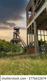 A disused coal mine pithead winding gear of an old Belgian coal mine shaft against a dramatic sunset sky