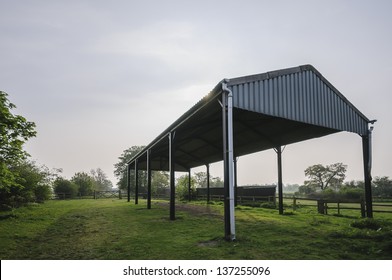 A disused farm building in Yorkshire, UK. It stands in a paddock surrounded by fences and gates. The metal structure backlit having been photographed contre-jour.