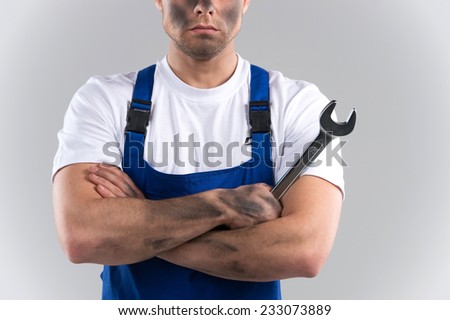 dity young mechanic in blue overall on blue background. closeup of man holding wrench and holding hands crossed
