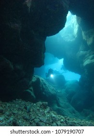  Diver with flashlight swimming through sunlit lava tube, Kona, Hawaii.                              