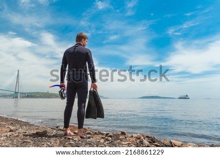 a diver in a wetsuit stands on the seashore. Diver before diving into the ocean, in the hands of a mask and fins for diving. High quality photo 商業照片 © 
