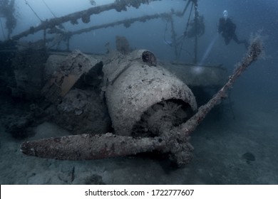 Divers Close In And Examine A WWII Fighter Plane Wreck At The Ocean Bottom