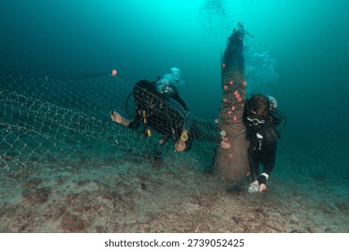 Divers work underwater to take away ghost nets tangled in coral reefs. This activity helps protect marine animals and improve the health of the reef ecosystem.