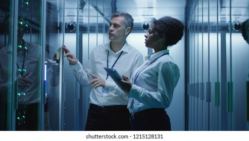 Diverse Adult Man And Woman Using Tablet And Laptop While Diagnosing Server Hardware In Modern Data Center