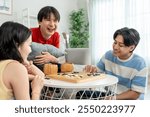 Diverse Asian young friends play board game Go in living room at home. Attractive young man, woman and lgbtq friend having fun, participate in traditional chinese board game match on table in house.