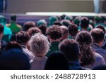 Diverse audience gathered and attentively listening during a conference or event, viewed from the back. Ideal for themes of education, business, and gatherings.