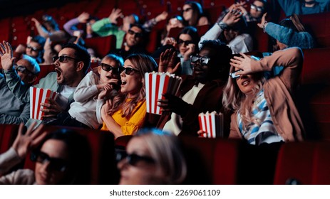 A diverse audience is in a movie theater watching a scary movie with 3D glasses, expressing fear. - Powered by Shutterstock