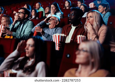 A diverse audience is in the movie theater watching a scary movie and gesturing in fear. - Powered by Shutterstock