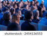 Diverse audience of professionals intently listens to a speaker at a conference event, capturing the essence of engagement and learning in a corporate environment.