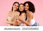 Diverse beauty. Portrait of happy black, asian and caucasian ladies posing together and smiling at camera over pink background, studio shot