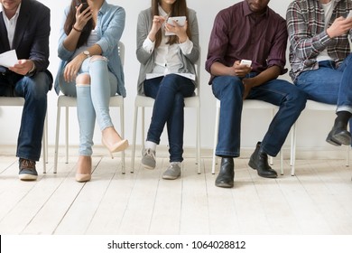 Diverse black and white people sitting in row using smartphones tablets, multiracial men and women waiting for job interview, human resources, employment or customers and electronic devices concept