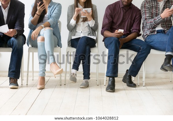 Diverse black and white people sitting in row\
using smartphones tablets, multiracial men and women waiting for\
job interview, human resources, employment or customers and\
electronic devices\
concept