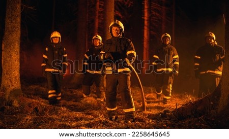 Diverse Brigade of Five Professional Firefighters Posing and Looking at Camera in a Forest Fire Situation. Multicultural Team Wearing Protective Clothing and Gear. Squad Leader Holding a Firehose.