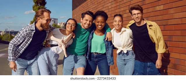 Diverse bunch of happy joyful friends hugging in the city street. Cheerful positive carefree young people in beautiful comfortable casual clothes meet up, enjoy free time and have fun together - Shutterstock ID 2273433433
