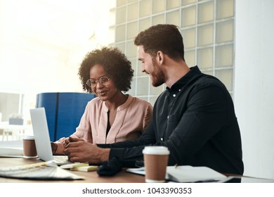 Diverse business colleagues sitting at a desk in a modern office talking together over a laptop 