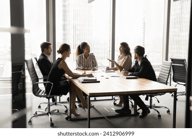 Diverse business partners meeting on serious conversation, talking at large table in modern office space with large urban window, discussing partnership, investment - Powered by Shutterstock