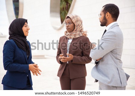 Diverse business partners meeting outside and discussing deal. Businessman and Muslim businesswomen standing outdoors and talking. Partnership and meeting concept