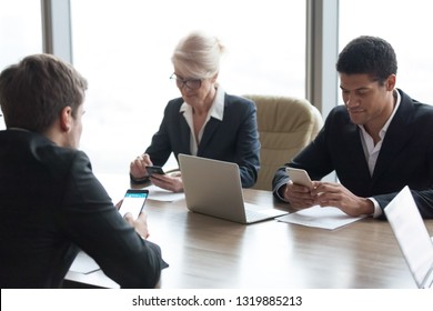 Diverse business people executives holding phones using smartphones apps at office meeting working on cellphones online, corporate employees businessmen and businesswomen lost in mobile gadgets - Shutterstock ID 1319885213