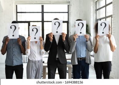 Diverse business people hiding faces behind papers sheets with question marks, standing in row in office. Identity and equality employee at work, candidates waiting for job interview, recruitment.
