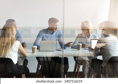 Diverse Business People Negotiate Sit At Conference Table Behind Closed Glass Door At Group Private Meeting, Multi Ethnic Team Staff Employees Talk At Briefing Discuss Work In Modern Office Boardroom