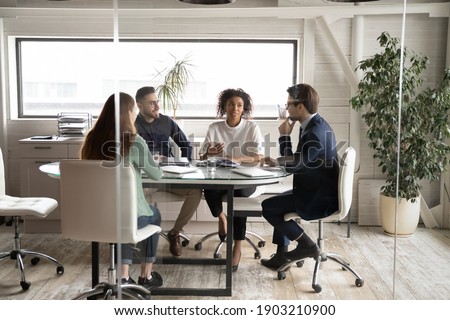 Diverse business people partners discussing project, contract terms, brainstorming in modern board room behind glass wall, colleagues sitting at table in office, talking, sharing startup ideas