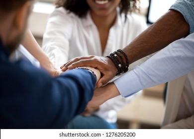 Diverse business people put hands together in stack pile as concept of team help, unity and teamwork, multi-ethnic students employees group engaged in teambuilding promising support, close up view