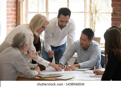Diverse business project team young and old workers brainstorm on paperwork talk engaged in teamwork at corporate briefing, serious staff people discuss work plan pointing at papers at group meeting