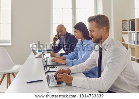 Diverse business research group using computers sitting at desk in company office. Team of young and old financial specialists working on laptops. Elderly executive manager supervising new interns