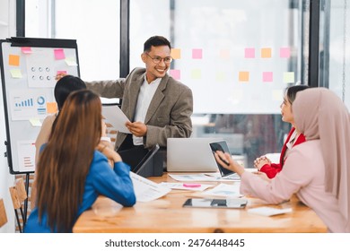 Diverse business team analyzing data and discussing strategies during an office meeting, using documents and a laptop. - Powered by Shutterstock