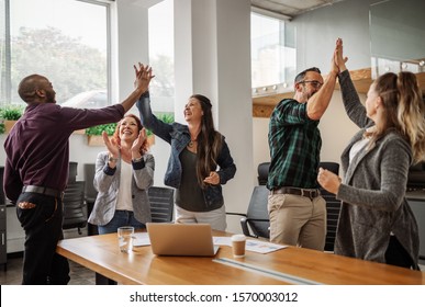 Diverse Business Team Celebrating And Giving High Fives During Boardroom Meeting