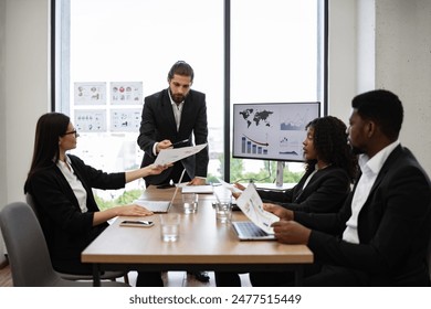 Diverse business team discussing financial graphs in modern office. Colleagues in formal attire collaborating on company strategy. Professional work environment with charts and statistics displayed. - Powered by Shutterstock