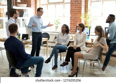 Diverse business team employees listening to male manager coach speaking at group office meeting, mentor executive leader talking during briefing, multi-ethnic workers engaged in corporate training