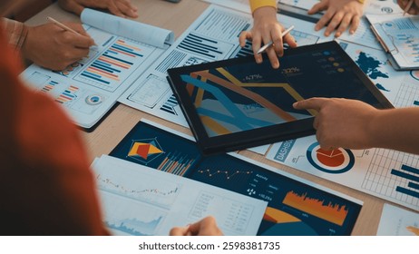 A diverse business team engages in collaborative work, analyzing charts and reports while using a digital tablet to drive strategic decisions in a modern office setting. SACTR