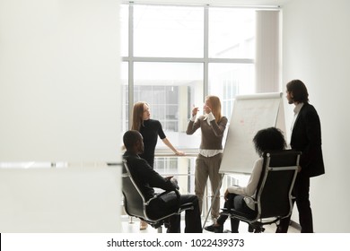 Diverse Business Team Listening To Female Speaker Discussing Presentation On Flip Chart At Meeting In Boardroom, Group Brainstorm And Marketing Sales Coaching Corporate Training Concept, Copy Space