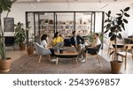 Diverse business team talking in modern co-working meeting space, sitting on couch, armchairs, using laptops, discussing work communication, teamwork, startup project strategy