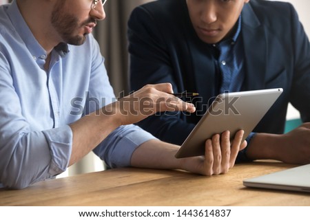 Diverse businessmen talking using digital tablet sit at office desk, male team two men working looking at tech device touchpad screen, corporate technology business apps concept, close up view