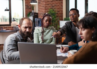 Diverse businesspeople looking at laptop computer analyzing company turnover working at marketing strategy during business meeting in startup office. Multiethnic team brainstorming ideas