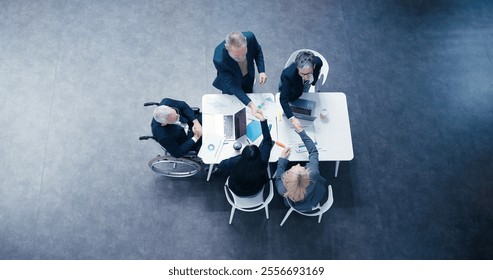 Diverse businesspeople stacks hands together celebrating success at board meeting. Man in wheelchair works at table with multiethnic colleagues upper view - Powered by Shutterstock