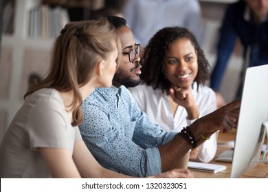 Diverse businesspeople working in shared office, focus on black american team leader sitting at desk together with females colleagues, mentor helps understand research data company corporate program