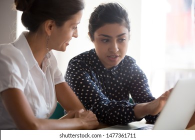 Diverse businesswomen discuss analyse online project look at laptop screen colleagues brainstorming strategizing together, mentor helping apprentice explain corporate program, support teamwork concept