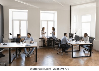 Diverse busy employees working on modern office room, sitting at workplaces, using desktops, talking, discussing project tasks. Contemporary rental office co-working space - Powered by Shutterstock